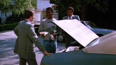 Zwei Männer im Anzug und Eddie Murphy am Kofferraum seines Autos.