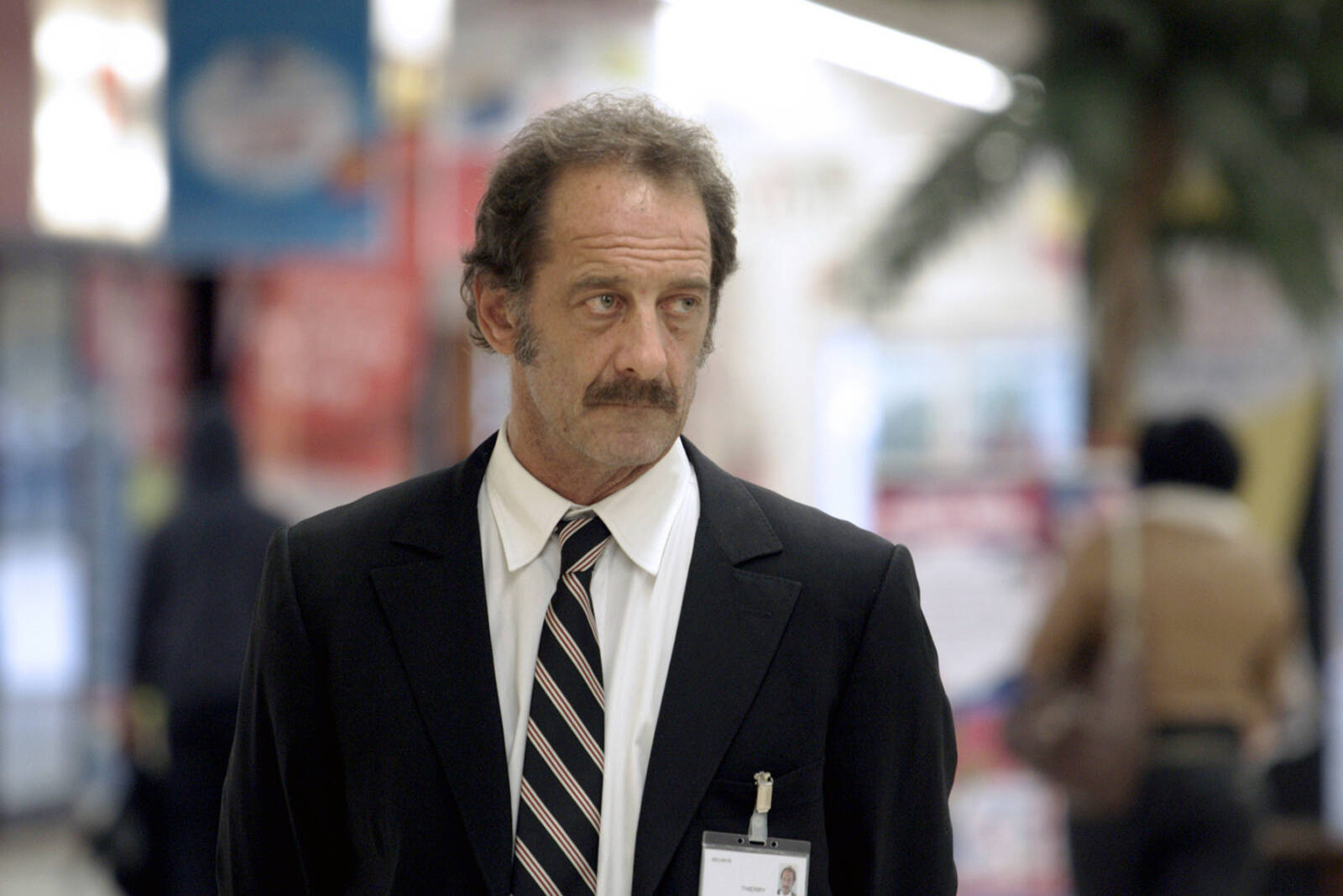 „Der Wert des Menschen“: Vincent Lindon in seiner Rolle als Ladendetektiv Thierry in einem schwarzen Anzug, mit weißem Hemd und gestreifter Krawatte.