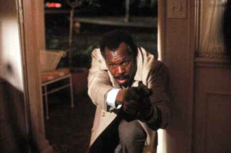 Danny Glover als Polizist Roger Murtaugh geht geduckt durch eine Tür mit einer ausgestreckten Pistole in den Händen.
