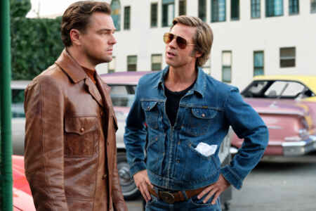 „Once Upon a Time in ... Hollywood“: Rick Dalton (Leonardo DiCaprio, l.) und Cliff Booth (Brad Pitt) in Kleidung der 60er stehen auf einem Parkplatz. Dalton schaut verzweifelt, Booth willensstark.