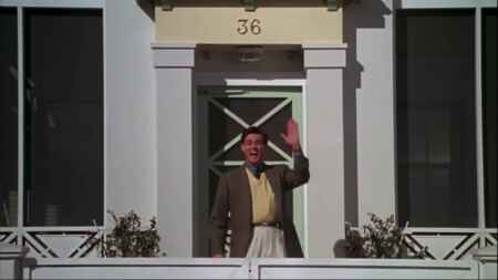 Jim Carrey winkt als Truman seinen Nachbarn zu, er steht vor dem Haus mit der Nummer 36.