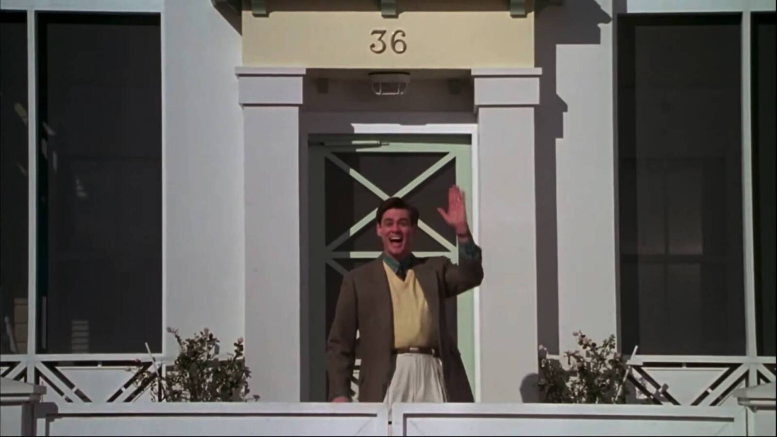 Jim Carrey winkt als Truman seinen Nachbarn zu, er steht vor dem Haus mit der Nummer 36.