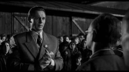 „Schindlers Liste“: Man sieht Liam Neeson als Oskar Schindler in einem Anzug mit Nazi-Brosche umringt von dankbaren jüdischen Arbeiter:innen (schwarz/weiß-Film).
