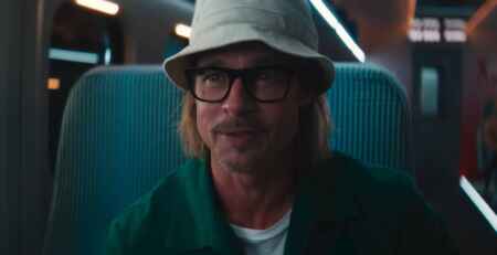 „Bullet Train“ Trailer zeigt Brad Pitt mit einem Anglerhut, einer schwarzen Brille und sitzend in einem Zugsitz, wie er lächelnd mit seinem Gegenüber spricht.