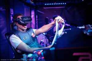 „Ghostbusters VR“: Man sieht einen jungen Mann mit VR-Brille in einem speziellen High-Tech-Sessel mit Lenkrad.