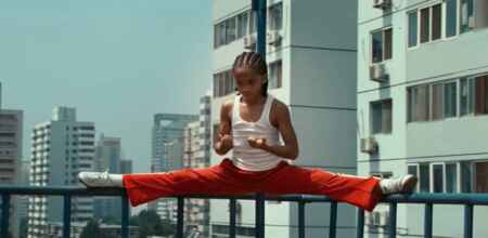 „Karate Kid“: Man sieht den 11-jährigen Jaden Smith, wie er Spagat auf dem Geländer eines Balkons macht (über Eck), im Hintergrund sind Hochhäuser zu sehen.