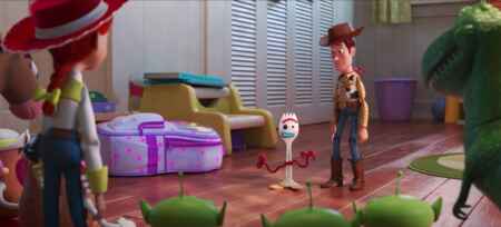 Im Vordergrund sieht man am Rand ein paar Spielzeuge von hinten, in der Mitte ist der Spielzeugcowboy Woody mit dem gebastelten Gabel-Spielzeug Forky zu sehen.