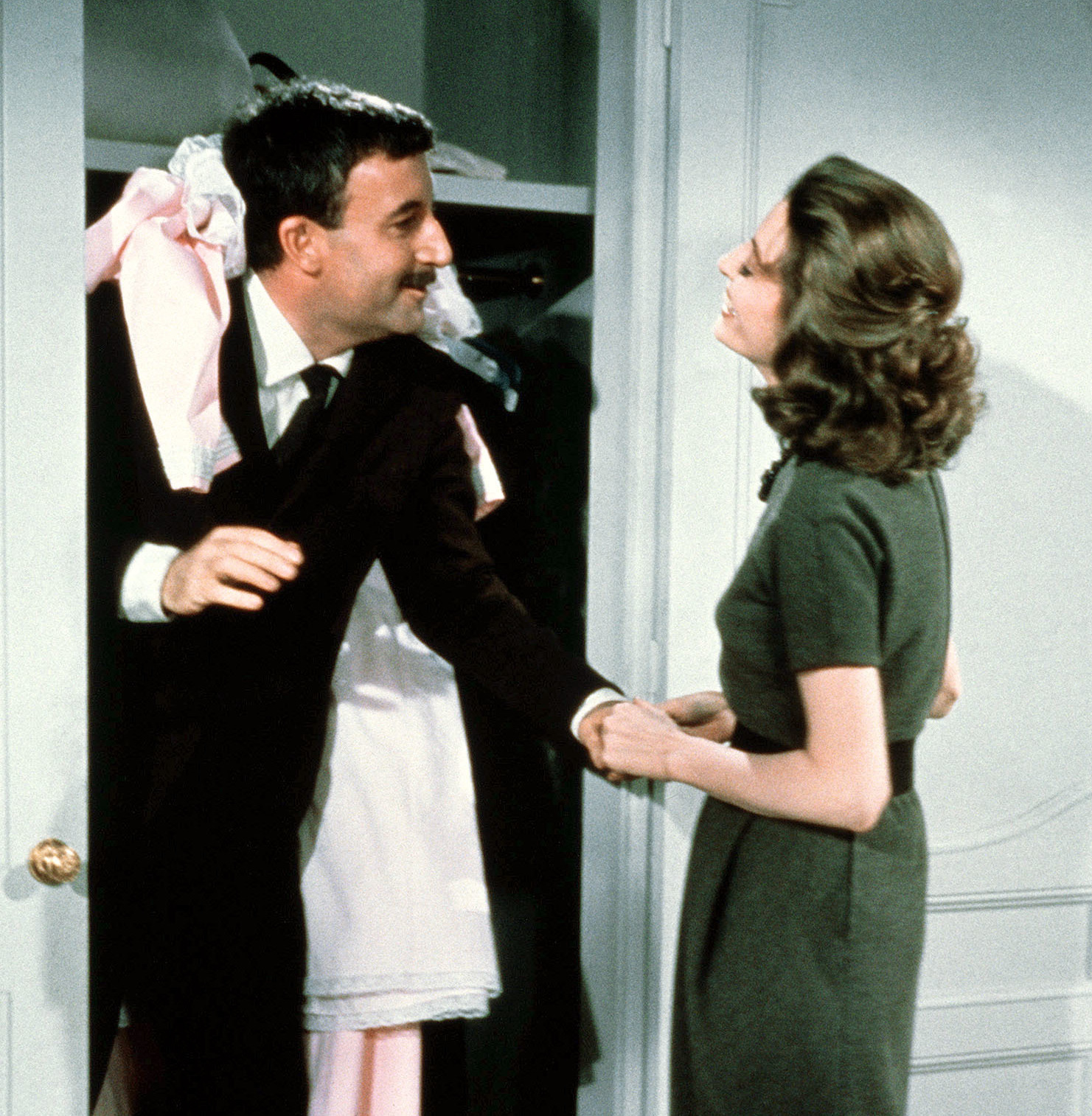 Inspektor Clouseau (Peter Sellers) ist mit kleidern übersäht und steht in der Tür eines Wandschranks, seine Frau Simone (Capucine) steht ihm gegenüber.