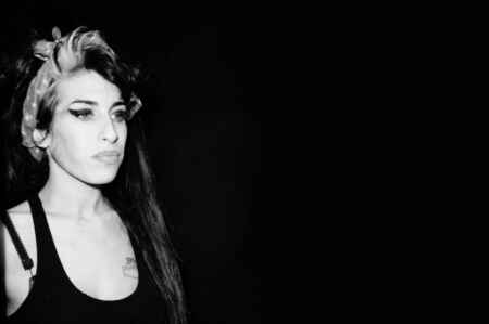 Amy Winehouse „Back to Black“: Man sieht Winehouse in der linken Ecke mit Haarband, schwarzem Top und typischem Liedstrich; es ist ein schwarz/weiß Foto, der Hintergrund ist schwarz.