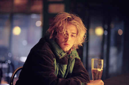 Zu sehen ist Xavier Dolan als Tom in einer Kneipe mit einem Glas Bier in der Hand, er sieht müde und niedergeschlagen aus.