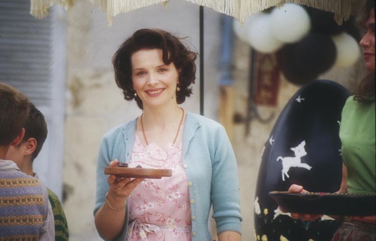 Juliette Binoche als Vianne vor ihrem Laden mit einem kleinen Teller Pralinen in der Hand.