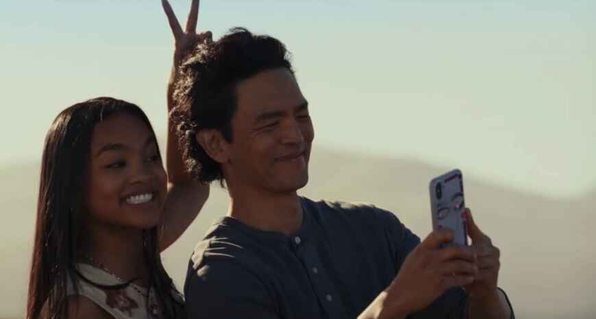 Man sieht Mia Isaac (l.) wie sie für ein Selfie lächelt und John Cho, der ihren Vater spielt und das Selfie aufnimmt, Hasenohren macht.