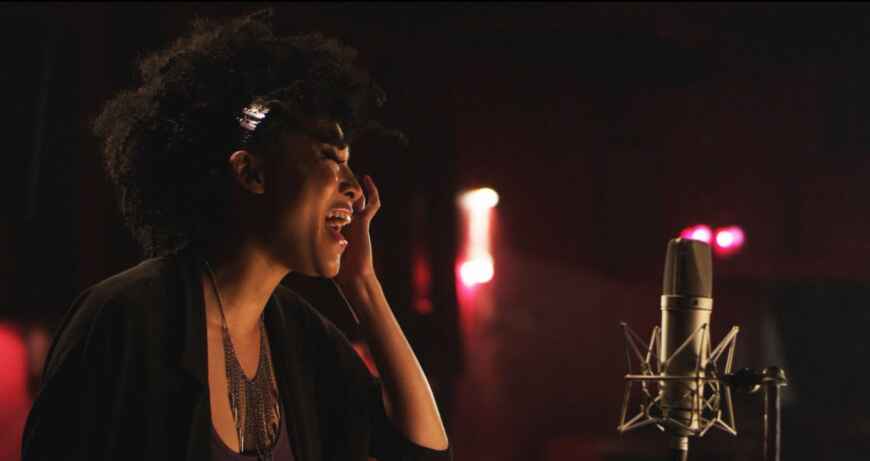 „20 Feet from Stardom“ im TV: Man sieht eine Sängerin von der Seite mit Kopfhörern, sie singt in ein Mikrofon in einem dunklen Aufnahmestudio.