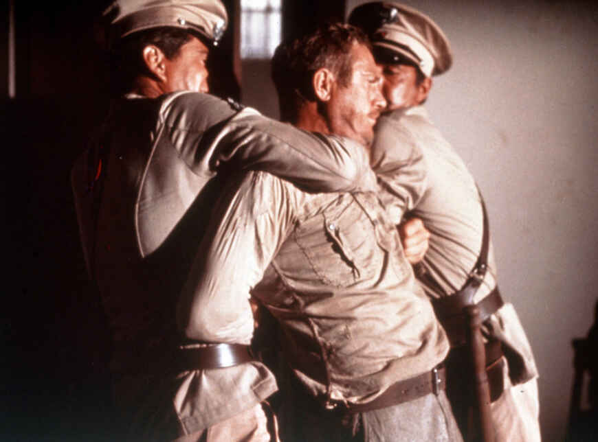 „Papillon“ im TV: Man sieht Steve McQueen als Gefangener Henri und zwei Wärter, die versuchen, ihn zu bändigen.
